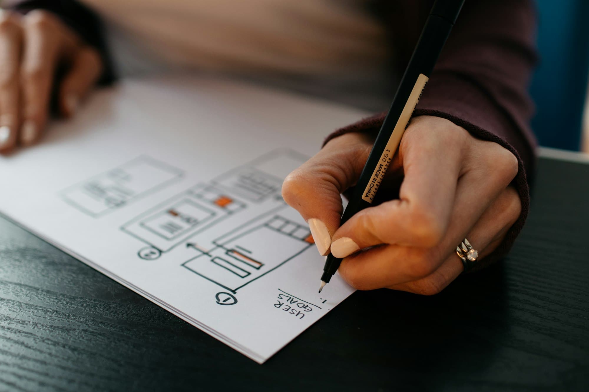 A hand sketches interface wireframes on paper during early planning.